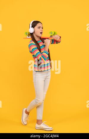 serious child in headphones with penny board. teen girl listen music. childhood activity. Stock Photo