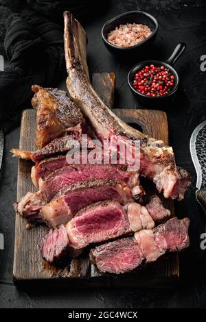 Traditional barbecue dry aged wagyu tomahawk steak sliced set, on wooden serving board, on black stone background Stock Photo