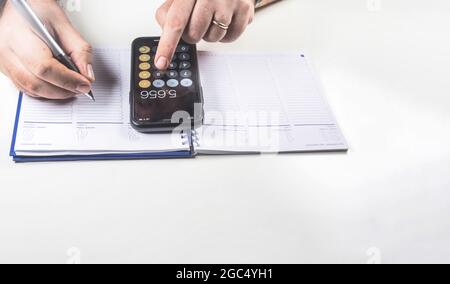 Man doing calculations with his mobile phone calculator and writing in a ring binder notebook with a pen. Budget and economy. Stock Photo