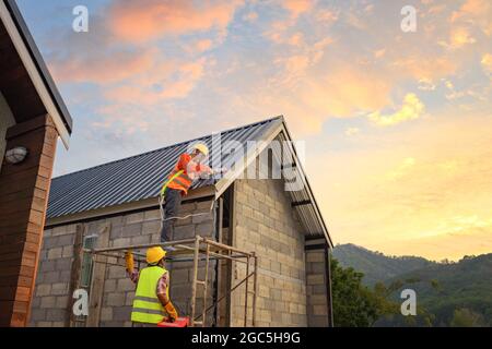 Roofer working on roof structure of building on construction site,Roofer using air or pneumatic nail gun and installing Metal Sheet on top new roof. Stock Photo