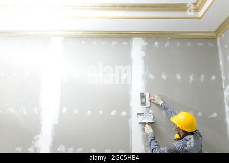 Putty plaster on the wall,Craftsman working with plaster gypsum ceiling for interior build gypsum board ceiling Stock Photo