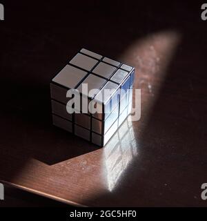 Mirror faces monotone Rubik's cube solved on tabletop with sunlight. Stock Photo