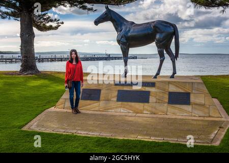 A female tourists stands beside the commemorative, bronze sculpture of race horse legend, Makybe Diva, in Port Lincoln in South Australia. Stock Photo