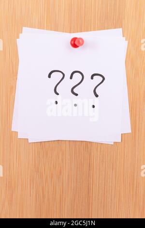 White Sticky Notes with Three Question Marks Pinned to the Wooden Message Board. To Do List Reminder in the Office. Memo Note at Work Stock Photo