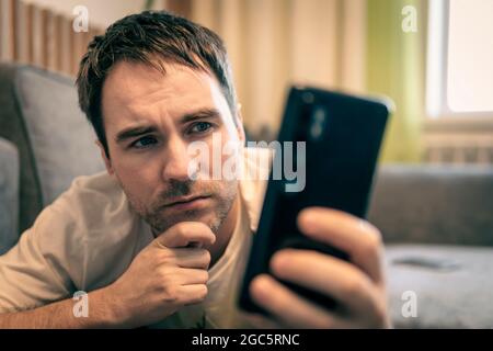 Middle age man using smartphone serious face thinking about question, confused idea. guy reads message on his smartphone sadly. man is resting and loo Stock Photo