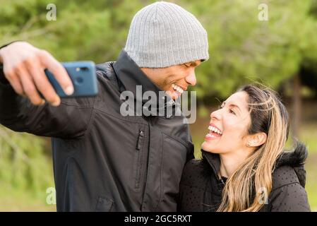Fitness couple in warm clothes taking a selfie in the park looking at each other Stock Photo