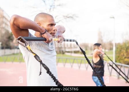 Atlhetic multi-ethnic people exercising arms with fitness strap in the park. Stock Photo
