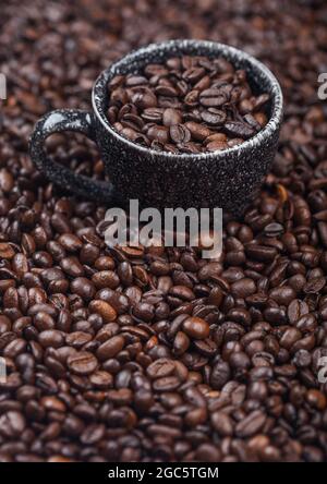 Black ceramic cup with fresh raw coffee beans inside beans background. Macro Stock Photo