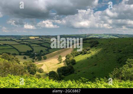 On a summers day in early August, the clouds part and the sun lights up 'The Punchbowl' and Winsford Hill on Exmoor National Park. Stock Photo