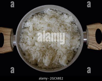 Bowl of cooked white long grain rice in a bowl with wooden handles and placed on a black counter top. Stock Photo