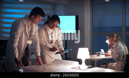 Man and woman in lab coats working in electronics lab with motherboard and control electronics scheme discussing the way of their improvement Stock Photo