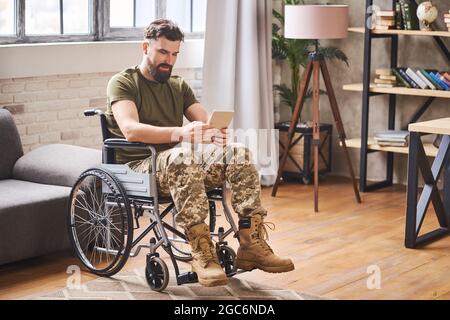 Disabled handsome military man sitting in a wheelchair and using a tablet Stock Photo