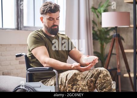 Depressed ex-serviceman sitting in a wheelchair and taking prescribed pills Stock Photo
