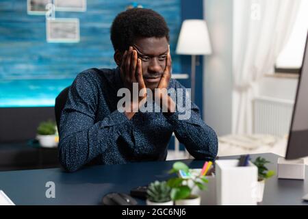 African american man having big headache from stress while rubbing his temples. Tired suffering black guy from working on assignment at office. Overwhelmed unhappy business person Stock Photo