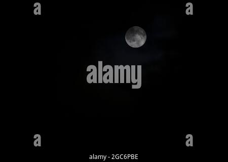 September Harvest Moon partially obscured by dark clouds Stock Photo
