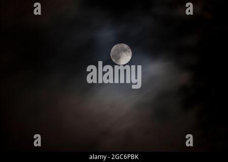 September Harvest Moon partially obscured by dark clouds Stock Photo