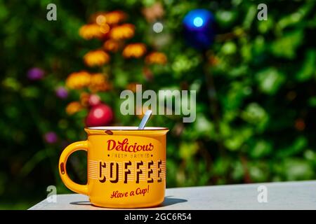 A yellow coffee cup on a garden table with blurred flowers in the background. Stock Photo
