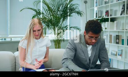 African-American man surfing laptop and sharing great news with coworkers sitting together in office around table. Stock Photo