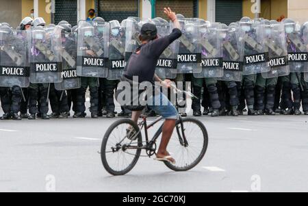 Bangkok, Thailand. 07th Aug, 2021. A protester rides a bicycle in front of riot policemen during the demonstration. The Metropolitan Police Bureau (MPB) will deploy at least 5,700 officers to ensure public order and security during the anti-government rally in the capital. The Free Youth group will gather at Democracy Monument on Ratchadamnoen Avenue before they march to the Grand Palace. Credit: SOPA Images Limited/Alamy Live News Stock Photo