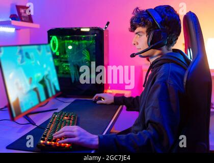 Caucasian young man in his room with colorful background plays video games on computer as hobby, entertainment and fun Stock Photo