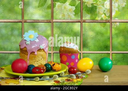 Easter still life. Easter cakes and colorful eggs on the background of a window in rain drops Stock Photo