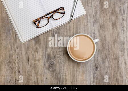 cup of coffee with a note book, reading glasses and a pen. Flat lay. Stock Photo