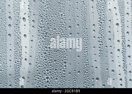 A small raindrop rests on the glass after rain. Raindrops On The Glass. Raindrops on the window. Blue tone. Abstract background. Stock Photo