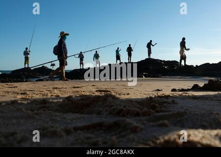 Fishing rod setup along the beach while a fisherman seeks his catch in the  sea Stock Photo - Alamy