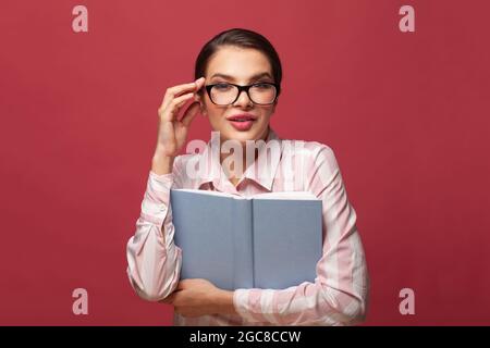 Surprised young woman brunette wearing glasses holding book with mockup copy space Stock Photo