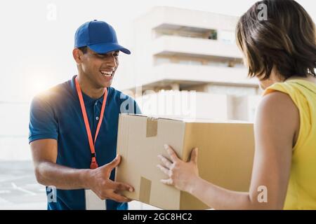 Hispanic courier man shipping cardboard box to customer client for fast delivery - Deliveryman giving package order to customer woman - Focus on guy f Stock Photo