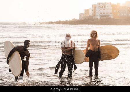 Multiracial surfer friends holding surf boards after extreme water sport session with beach on background -Soft focus on hipster senior man Stock Photo