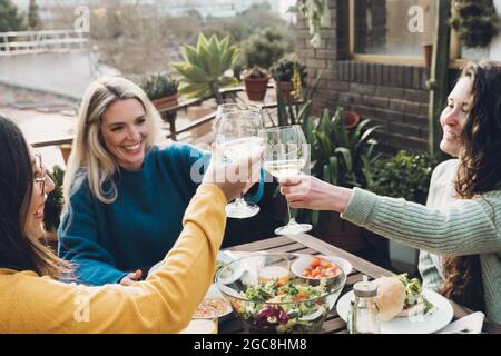Multiracial friends eating vegan food cheering with wine outdoors during summer at patio restaurant - Focus on african girl face Stock Photo