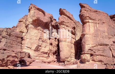 tiny tourists looking up at the majestic Solomons Pillars sandstone formation in Timna Park in Israel with a clear blue sky background Stock Photo