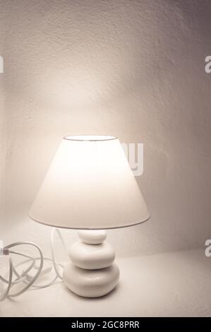 Close-up of burning lamp on nightstand. White stone wall. Stock Photo