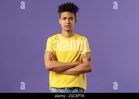 Close-up portrait of skeptical, unimpressed young man with dreads, look judgemental and uninterested, cross arms chest, go on impress me, smirk Stock Photo