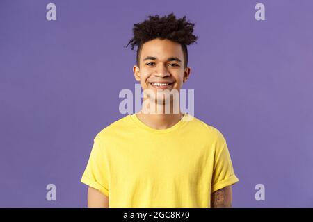 Close-up portrait of nice, friendly-looking hispanic male student in yellow t-shirt, grinning delighted, look upbeat happy and positive, standing Stock Photo