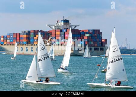 Flying fifteens before the start of their race during Cowes Week on the Isle of Wight with the COSCO container ship heading for Southampton. England Stock Photo