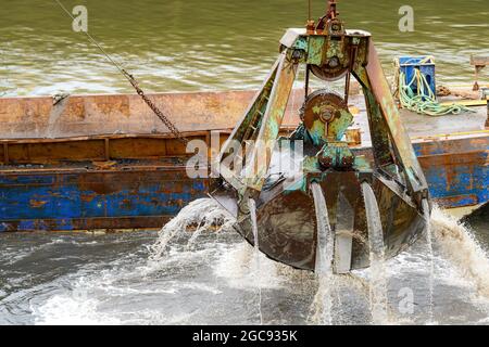 Closeup view of a large dredge scoop rising from the harbor. Water flows from it. Barge close behind. lots of detail, focus on scoop. Stock Photo