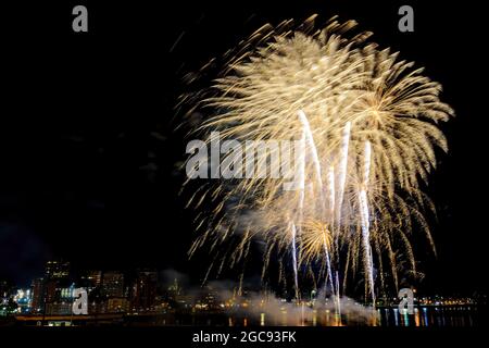 Bright fireworks explode over a city. Fine streamers with lots of detail. City lights any buildings behind. Stock Photo
