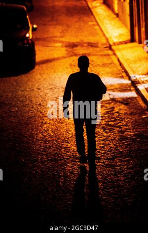 Back view of a man walking alone at night in a cobblestone alley Stock Photo