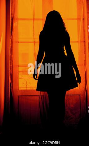 Silhouette of a woman in a dress in front of balcony door Stock Photo