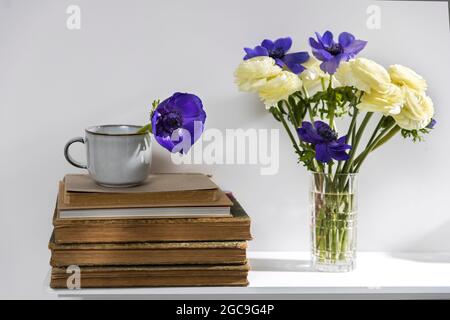 One blue anemone in a cup in the style of the seventies on the table with books as an interior decoration. Stock Photo