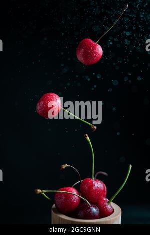 Collection of fresh cherries on a dark background, dynamic shot with action, splash, water drops and bokeh. Fresh fruit floating or levitating shotwit Stock Photo