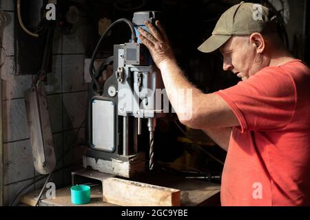 A man installs a drilling machine. The guy in the workshop is setting up the equipment. A machine for making holes in metal. Stock Photo