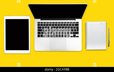 Computer, tablet and notebook on a solid yellow background. Minimalistic flat lay composition. Stock Photo