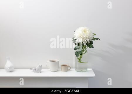 A large chrysanthemum in a glass vase, two fluted cups of coffee and ceramic bird figurines on the table. Office decoration. Stock Photo
