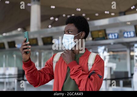 African man using face id feature on smartphone in medical mask in airport at covid-19 quarantine Stock Photo