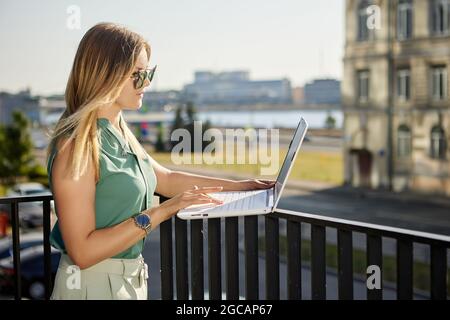 Woman is using laptop for working outside on balcony. Stock Photo