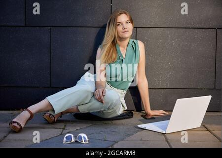 Young caucasian woman with laptop sits outside. Stock Photo
