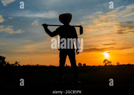 Male farmer holding a hoe in a field at sunset Stock Photo